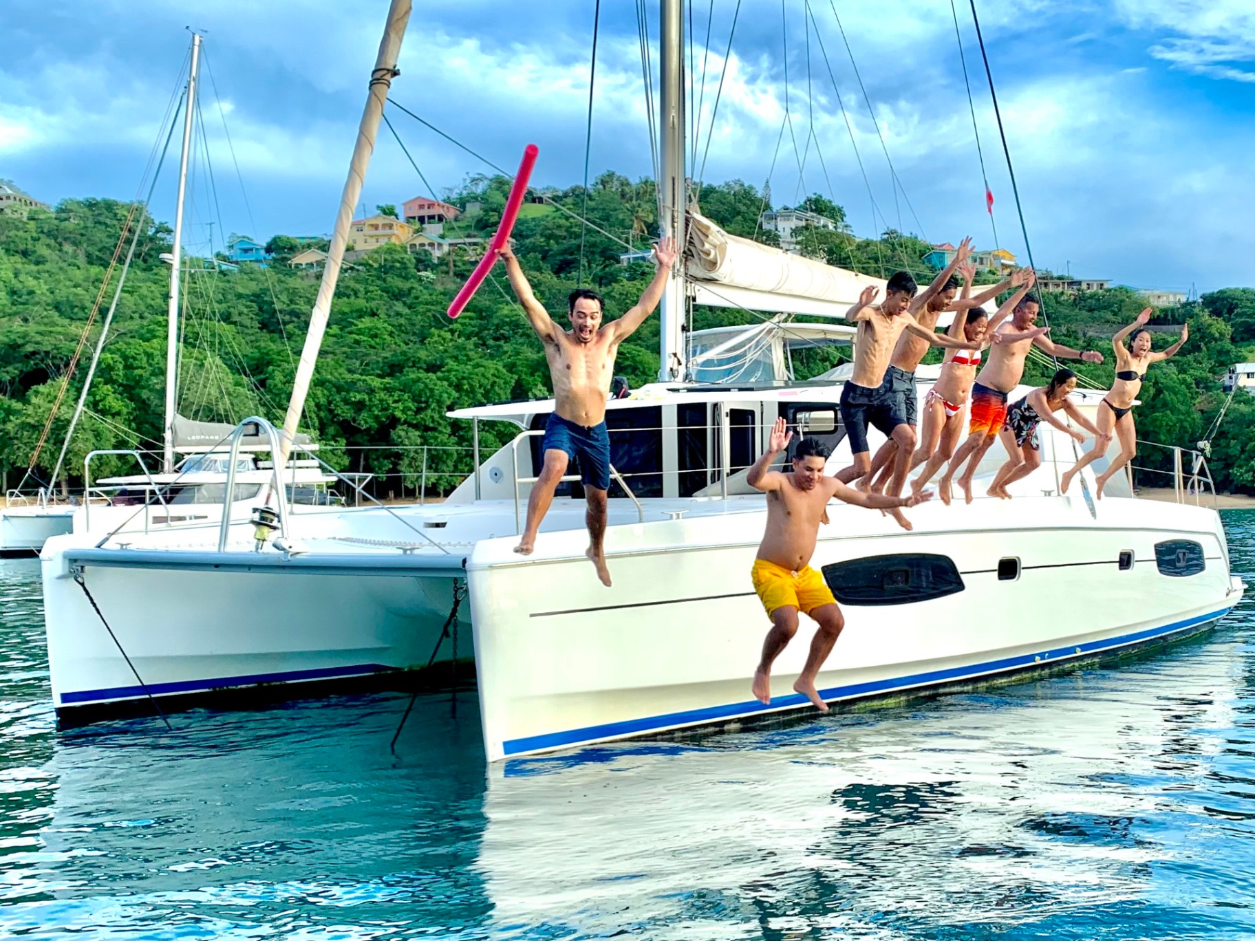 Family and friends jumping off the side of a catamaran into the sea